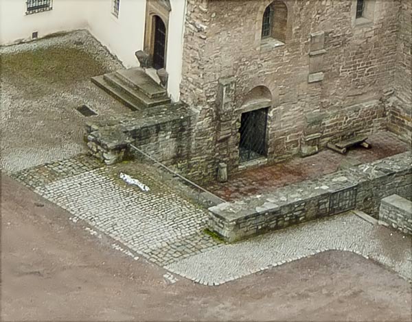 Blick vom Bergfried auf die Burgkapelle, das Pflaster verdeutlicht den Verlauf der Fundamente. Im Vordergrund die durchlaufende Nordwand. Die Südwand (an der Treppe zum Portal des "Krummen Hauses") ist nicht durchgängig, hier ist der Chor eingezogen.